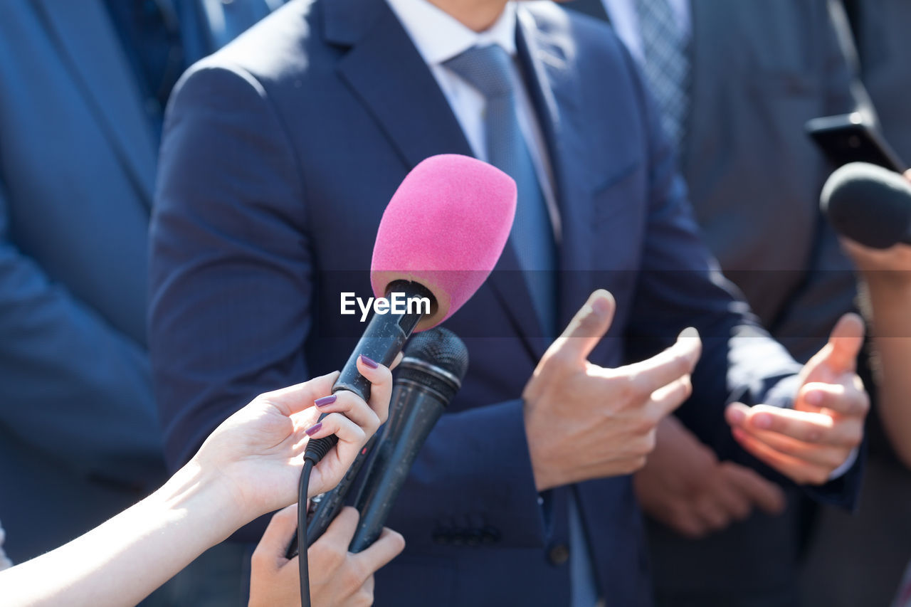 Cropped hand of journalist holding microphone in front of businessman