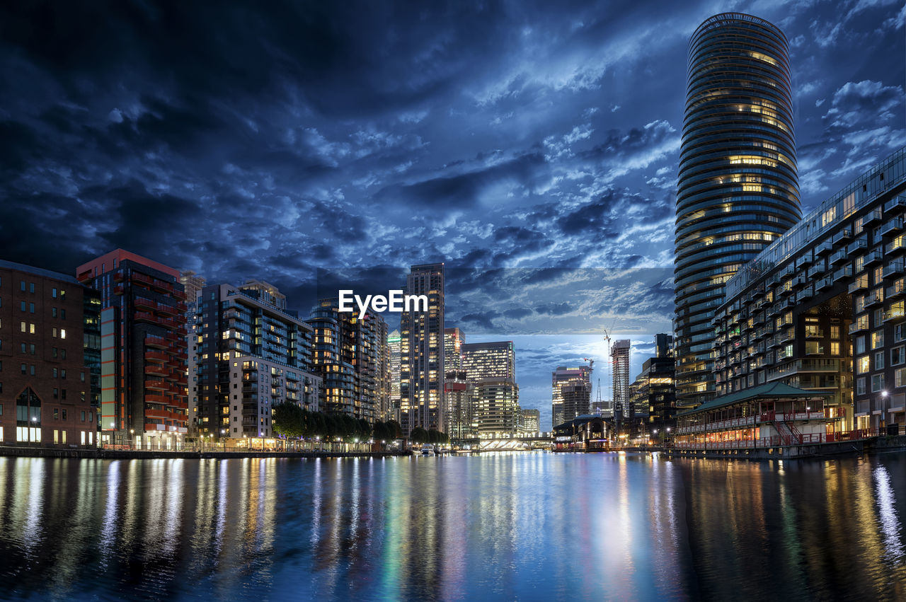 Low angle view of illuminated modern buildings by river in city against sky at night