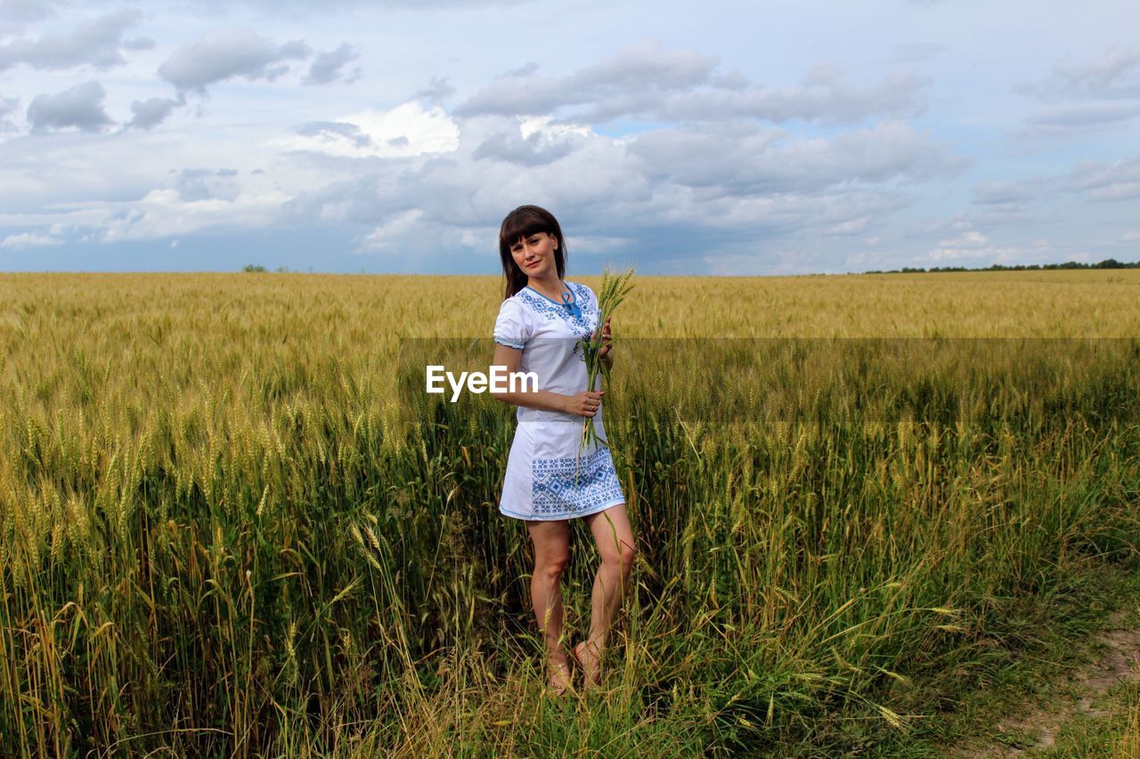 Portrait of young woman standing on landscape against cloudy sky