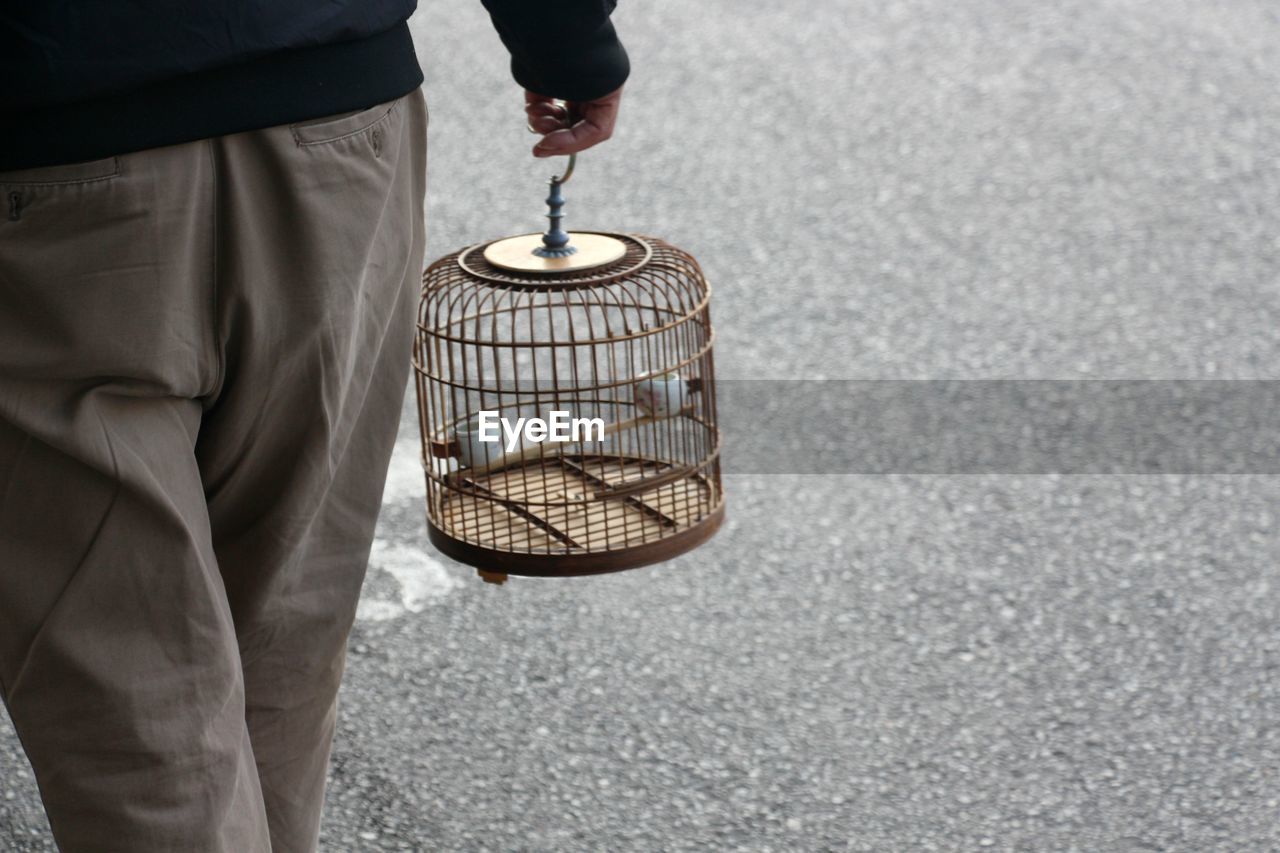 Midsection of person carrying bird cage on footpath