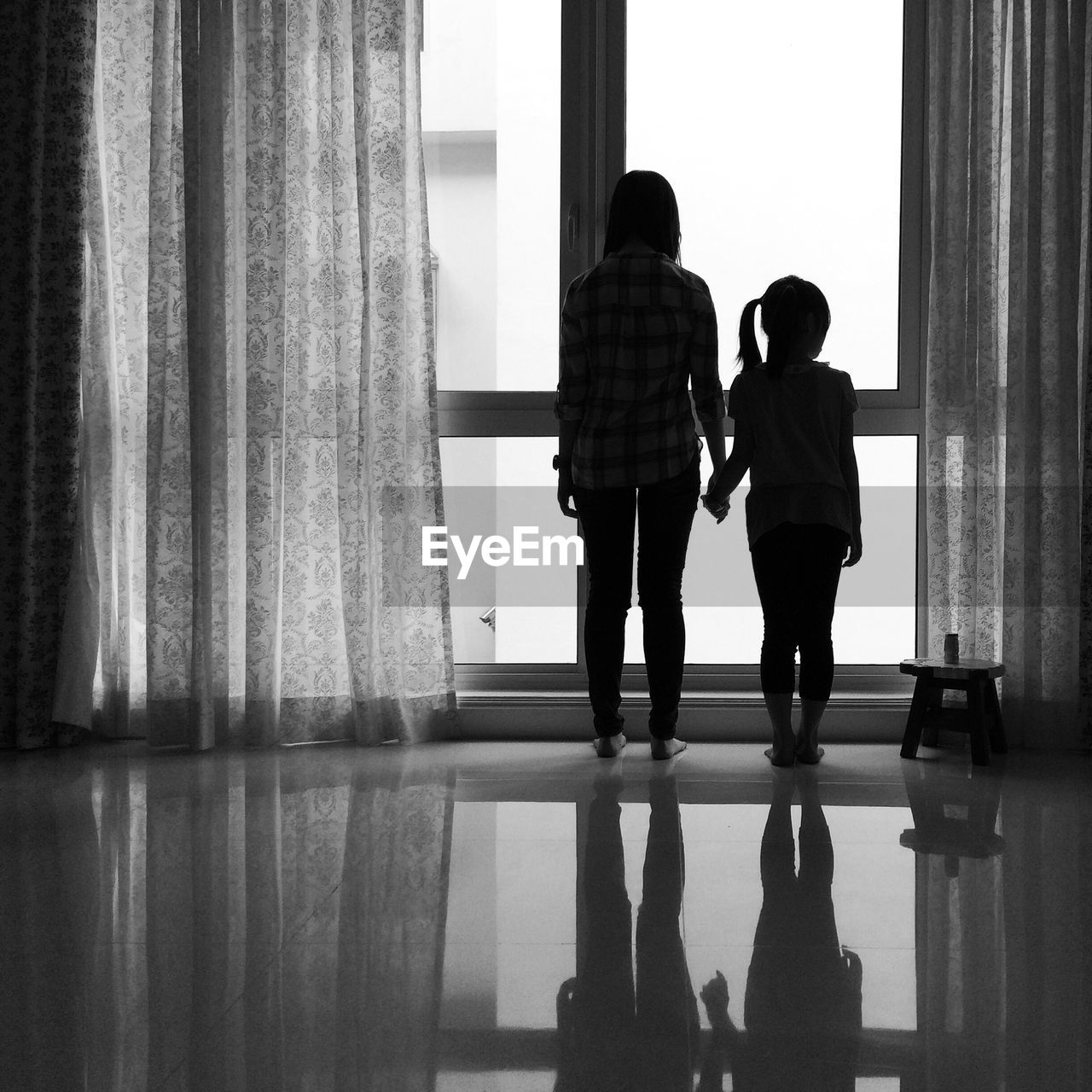 Rear view of siblings standing on floor by window at home