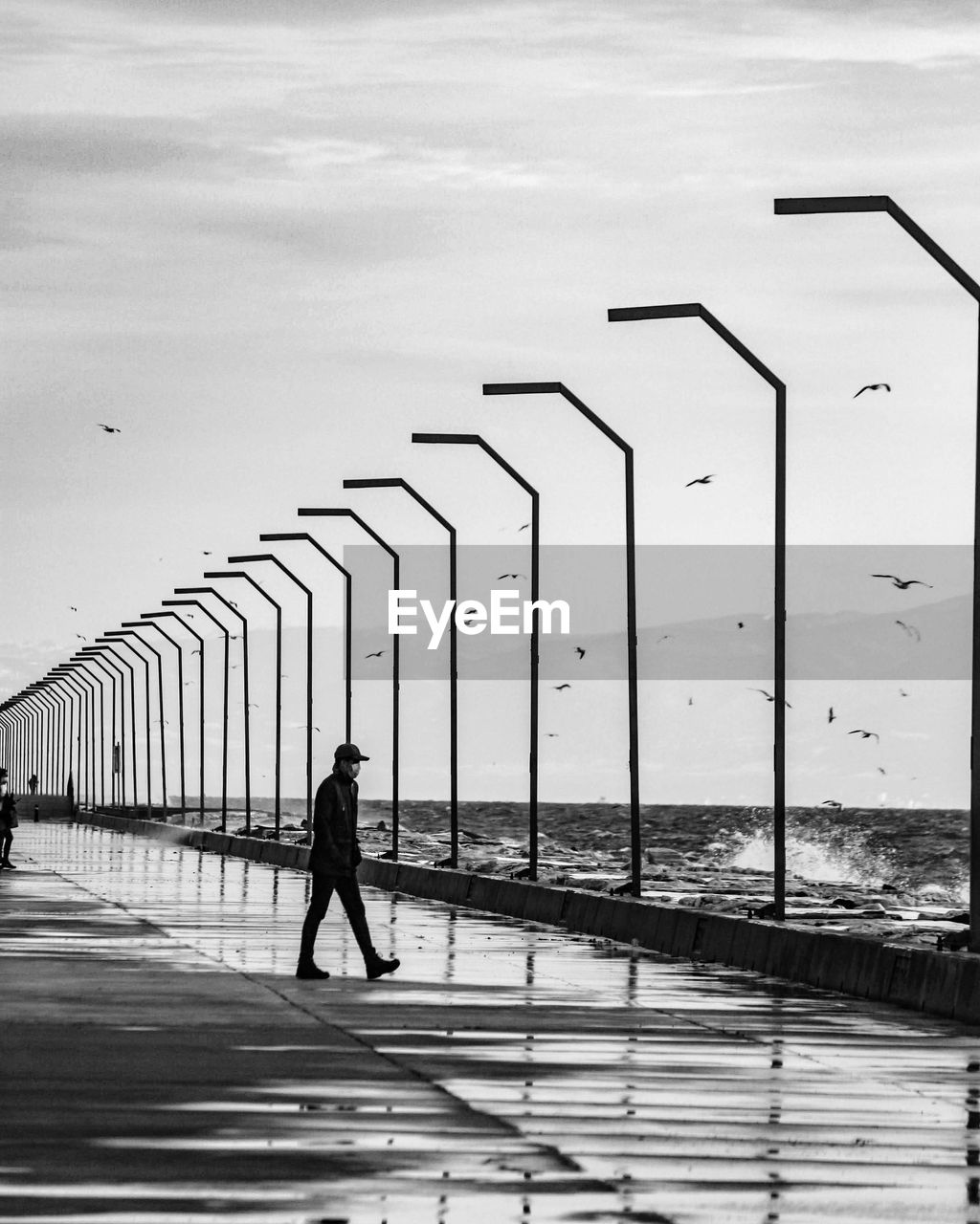  black and white rear view of man walking on bridge
