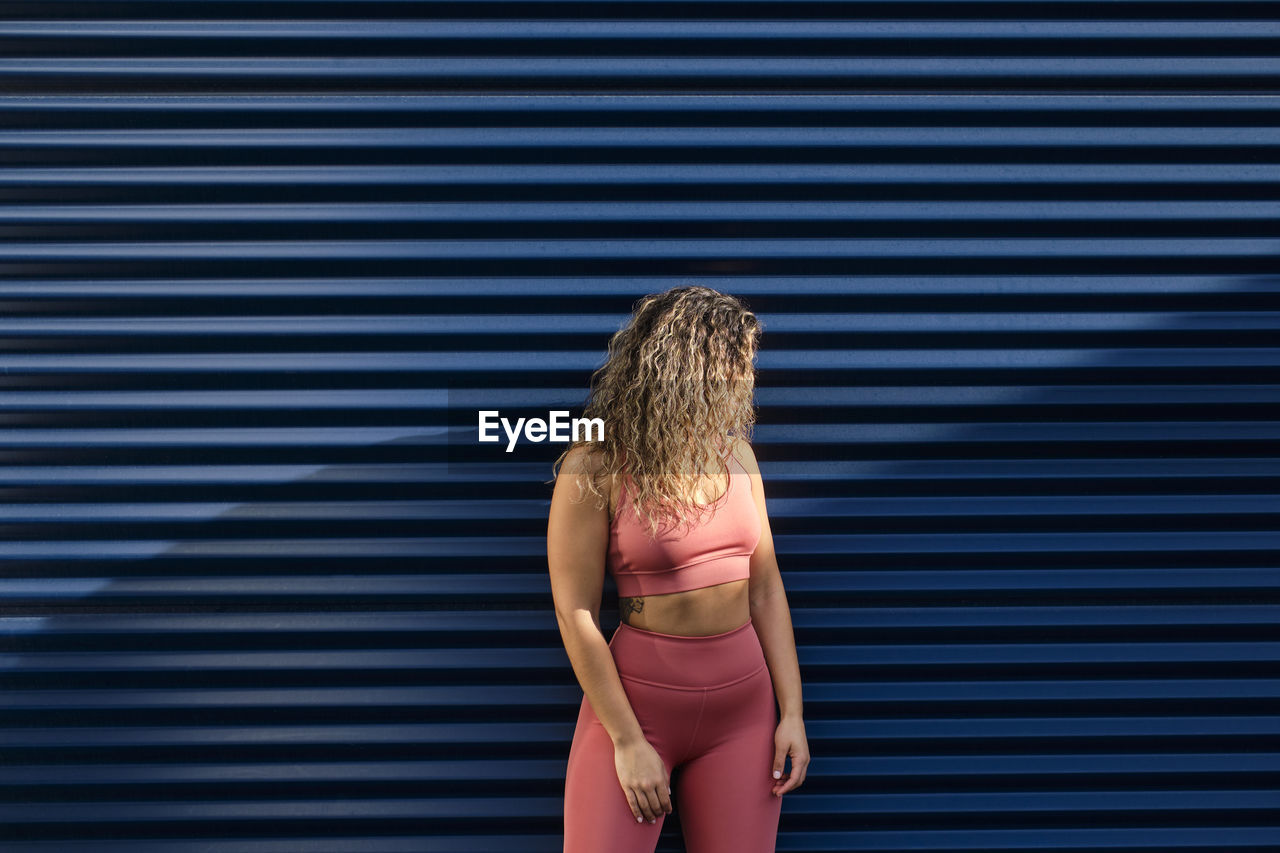 Young sportswoman with curly hair standing in front of blue wall