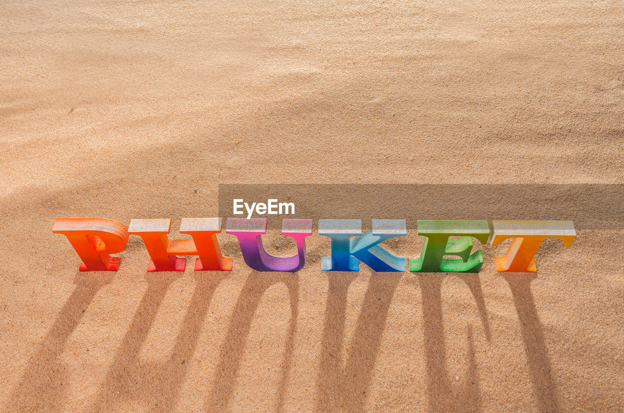 HIGH ANGLE VIEW OF MULTI COLORED TEXT ON SAND