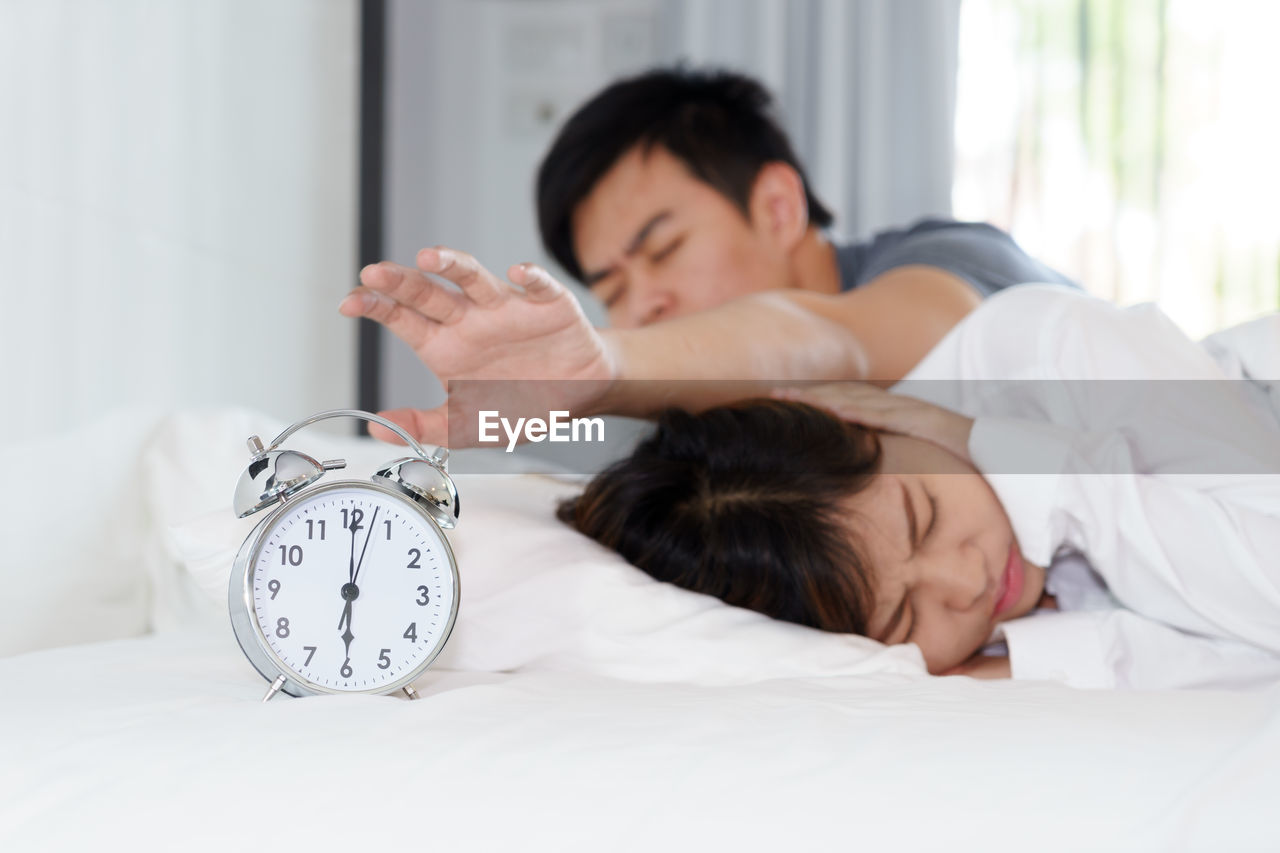 Man hand reaching towards alarm clock by woman on bed