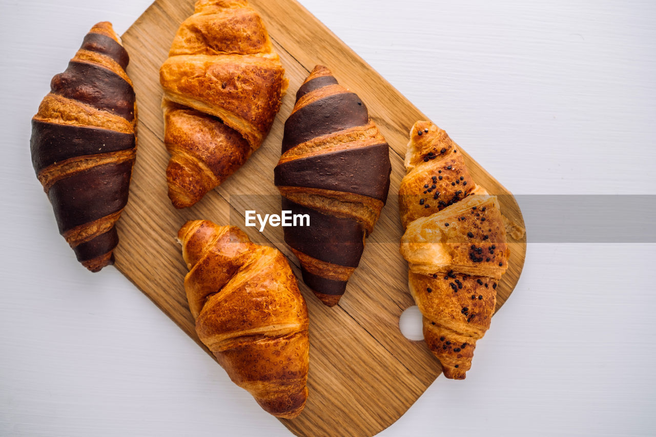 Flat lay of bunch of appetizing brown and chocolate croissants on a wooden board on white table