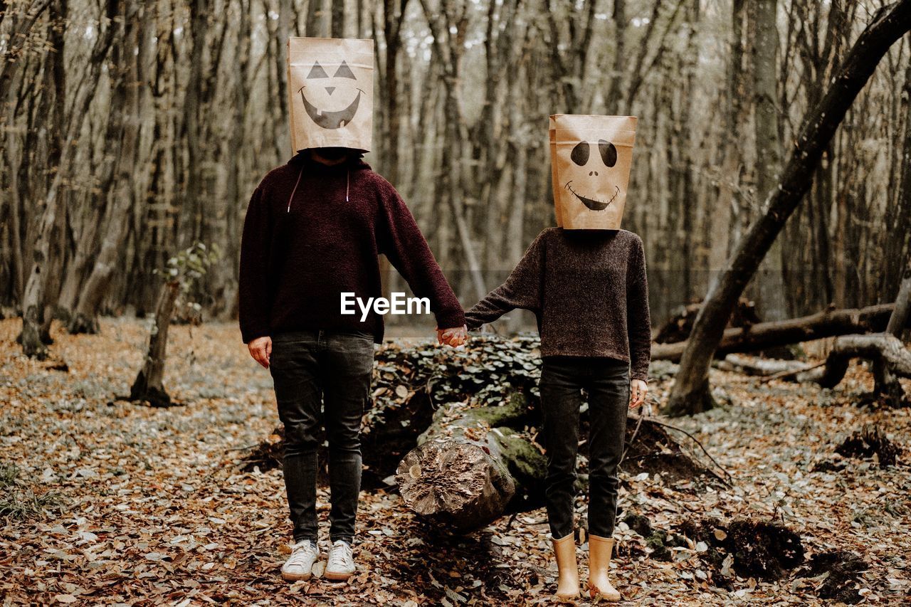 Rear view of friends standing by tree trunk in forest in halloween day