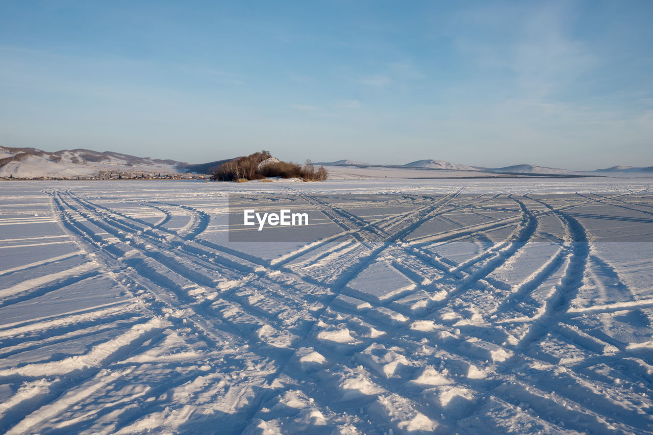 Car tracks go across the frozen great lake to the island against the backdrop of the village.