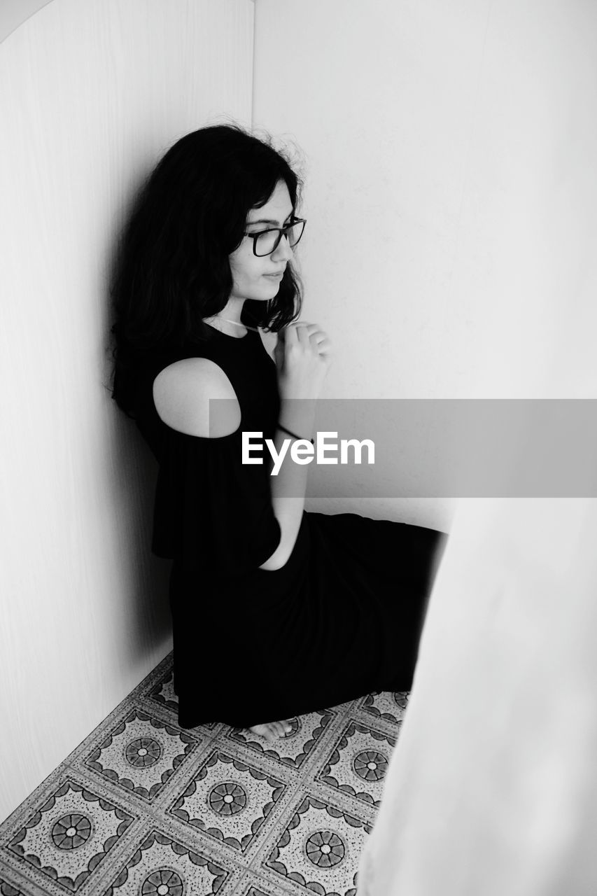 Young woman looking down while sitting against wall at home