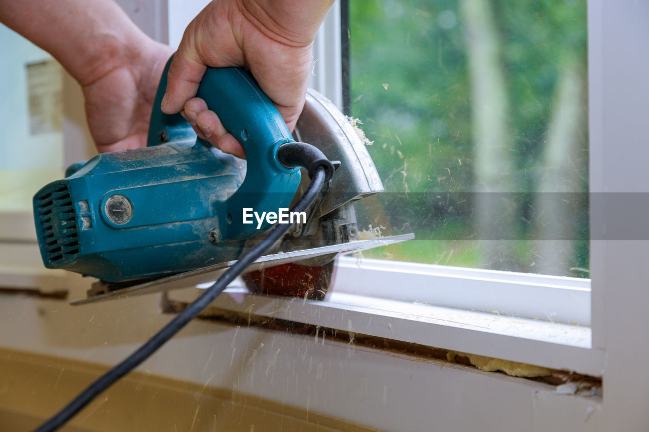 Cropped hand of carpenter working by window at home