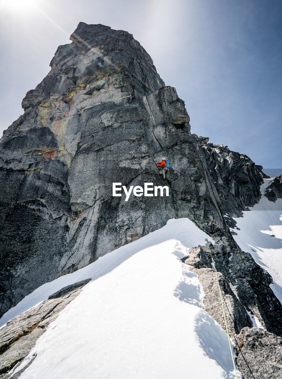 Male rock climbing giant peak in snow