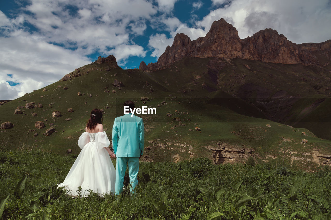 Bride and groom holding hands near a mountain against a cloudy sky in a natural park. a wedding