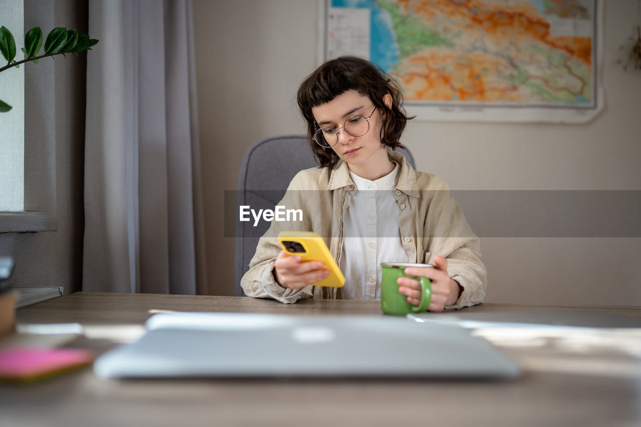 portrait of young woman using mobile phone while sitting on table at home