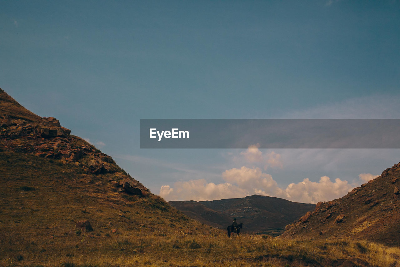 Man riding horse on mountain against sky