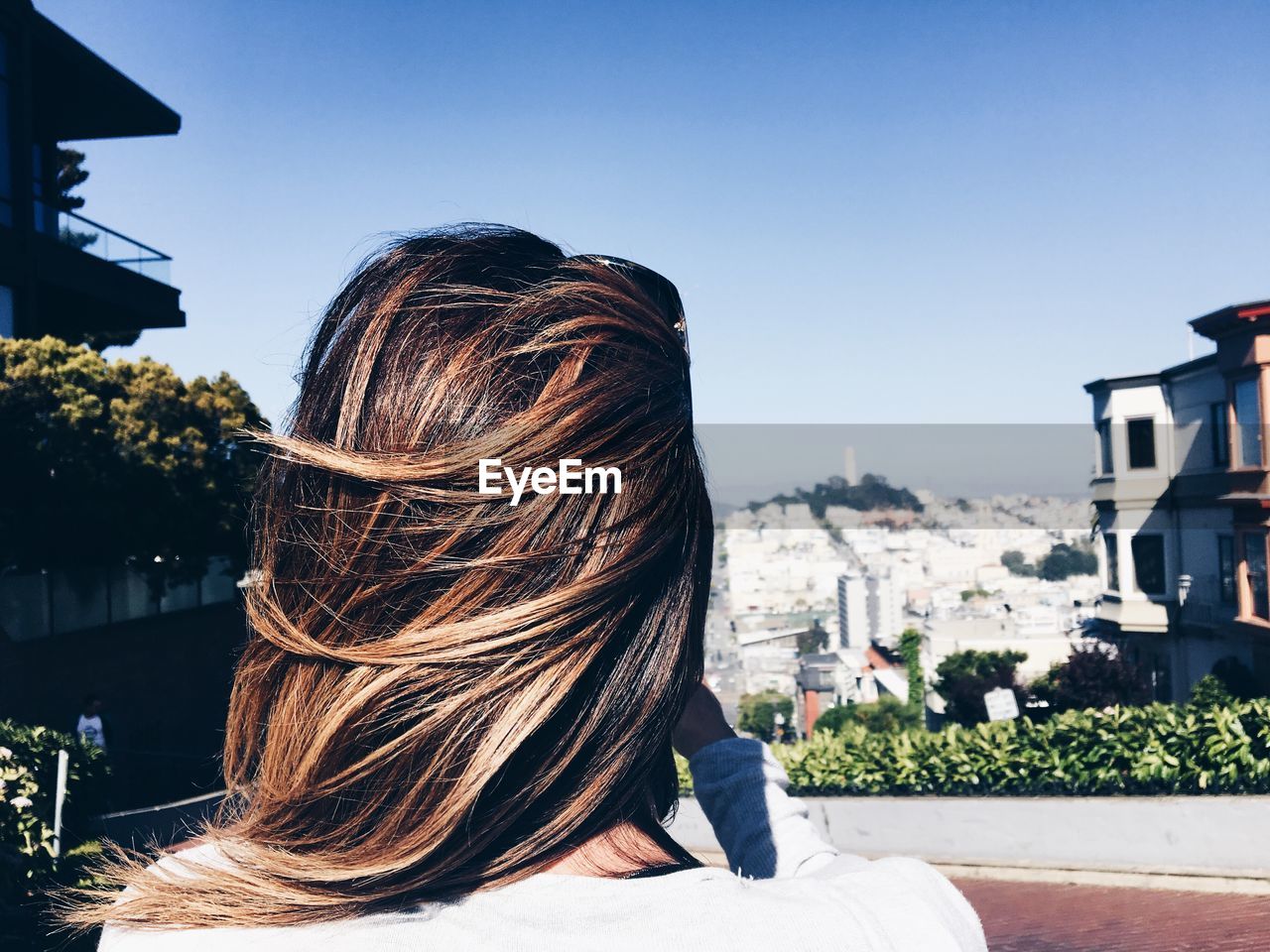 Rear view of woman with brown hair in city against sky on windy day