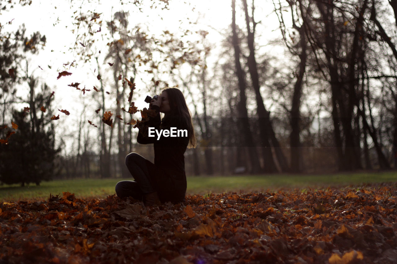 Woman photographing on field against trees