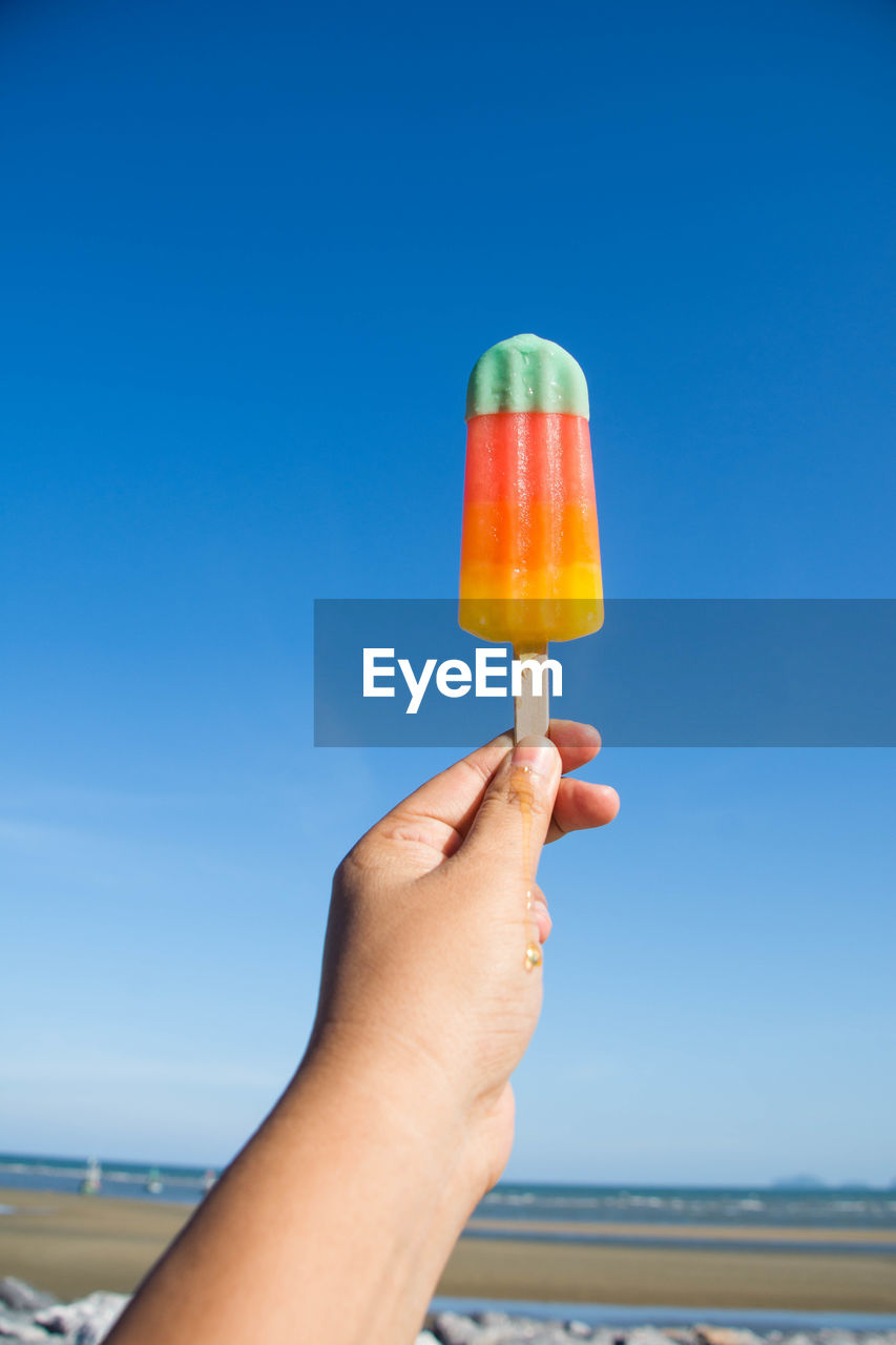 Close-up of hand holding popsicle against blue sky