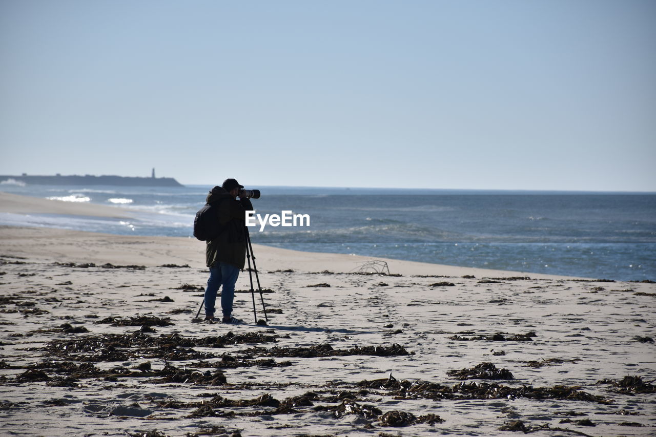 FULL LENGTH REAR VIEW OF MAN PHOTOGRAPHING SEA