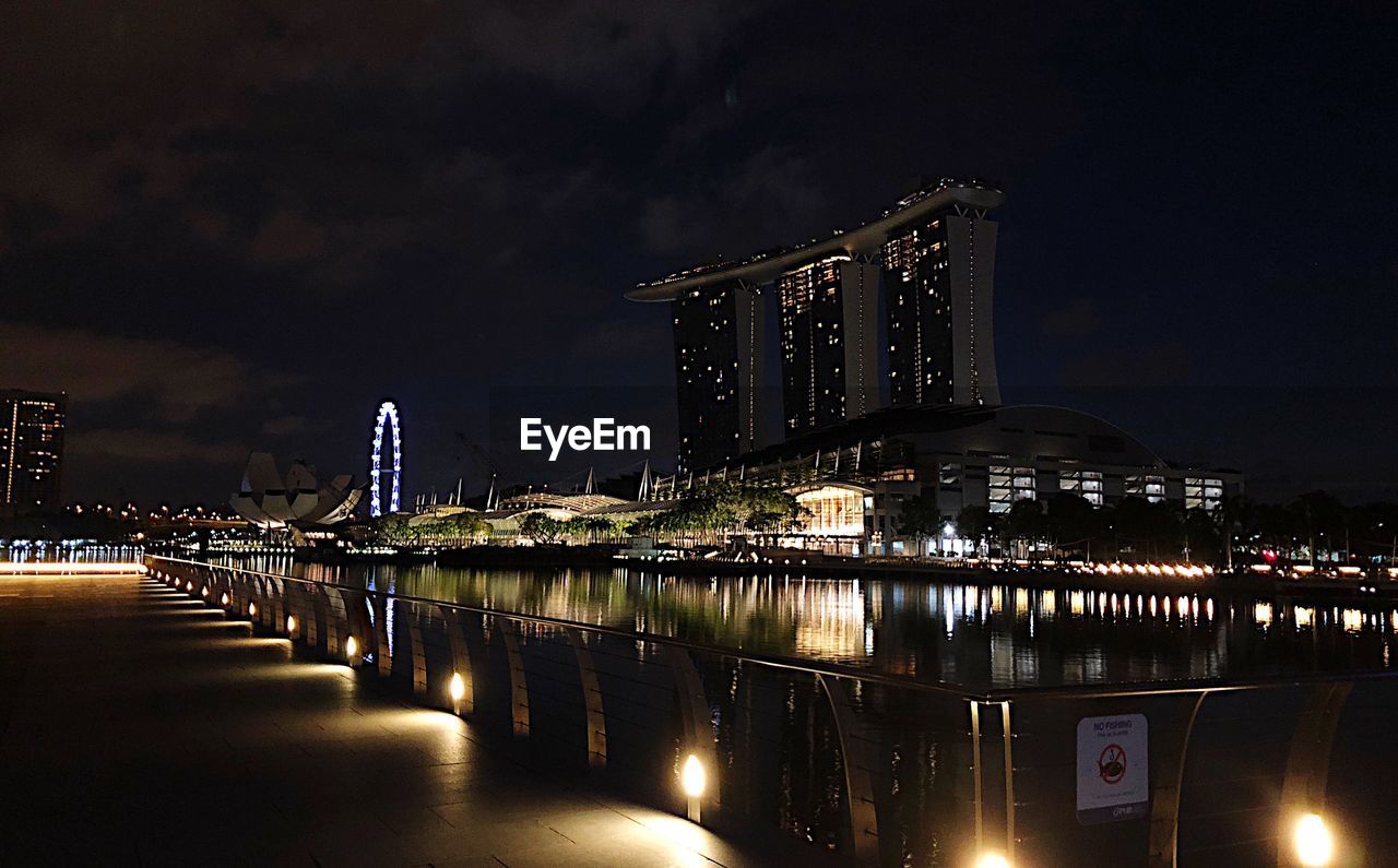 ILLUMINATED BRIDGE OVER RIVER WITH BUILDINGS IN BACKGROUND