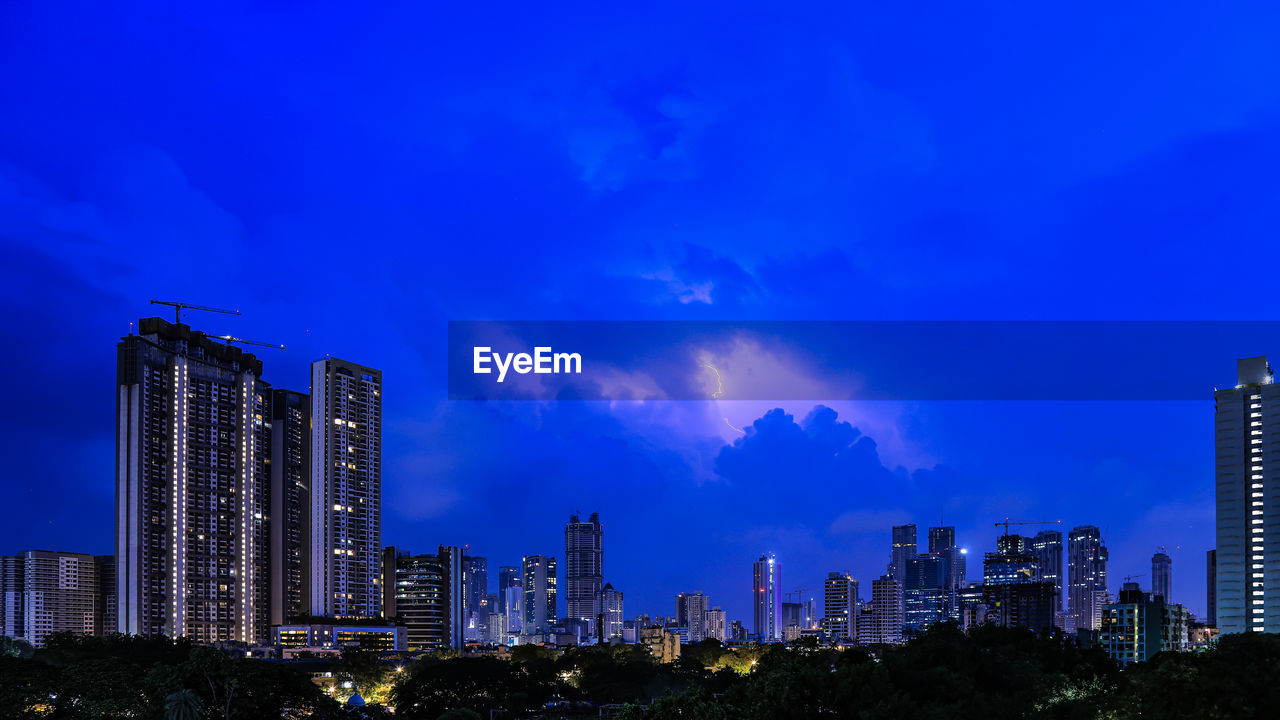 Panoramic view of illuminated buildings against sky at night further enhanced by  stunning lightning 