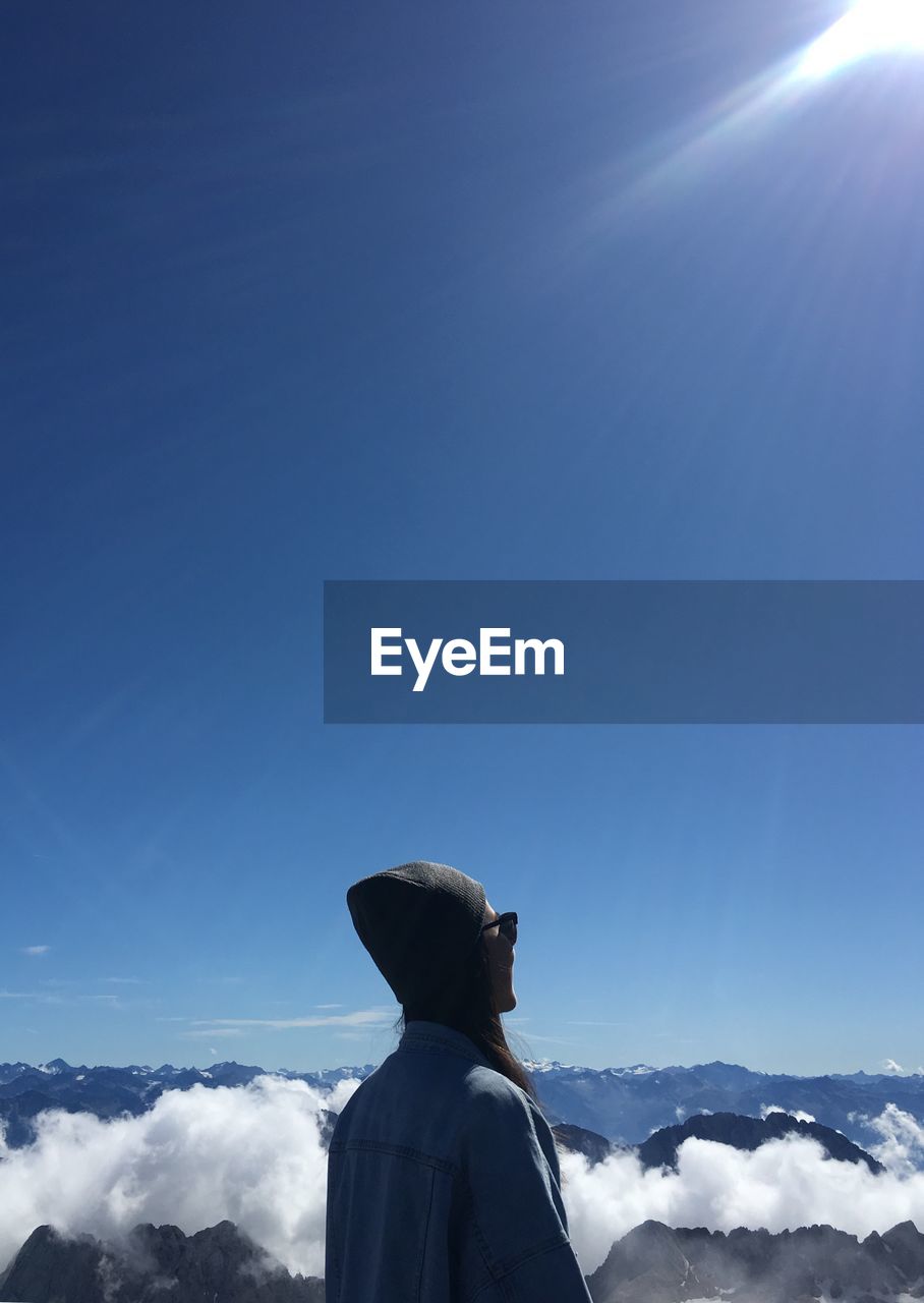 Woman looking at clouds covered mountain against blue sky during sunny day