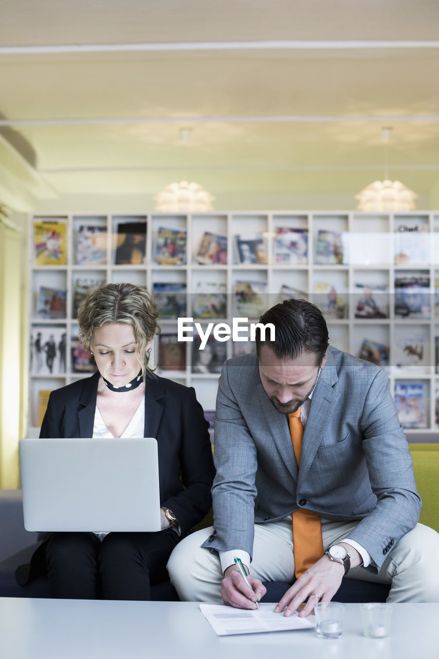 Mature businesswoman using laptop while colleague signing document in creative office