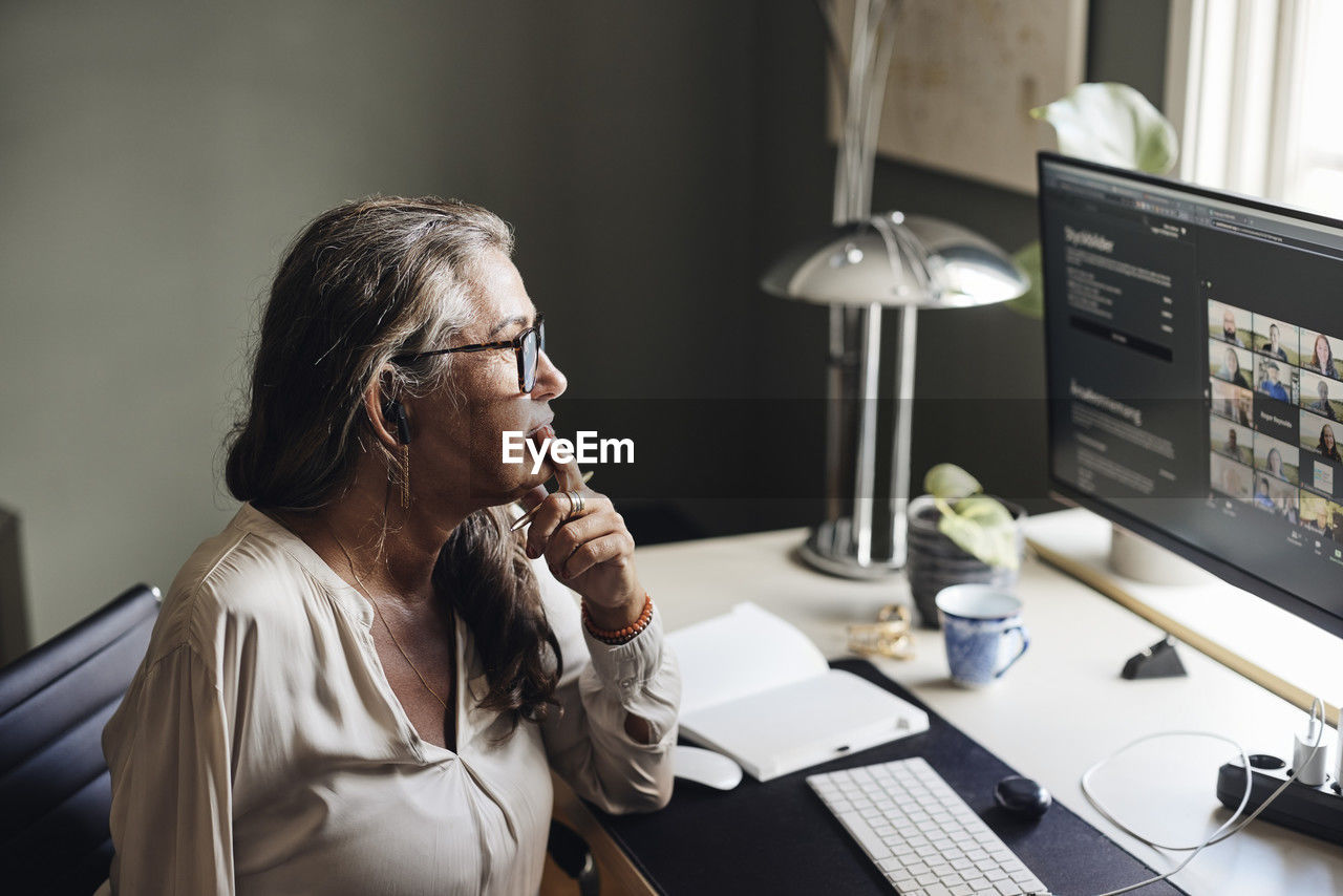 Businesswoman with hand on chin during video conference on computer at home office