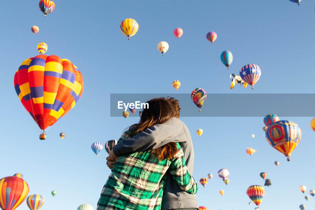 Low angle view of couple embracing against hot air balloons in sky