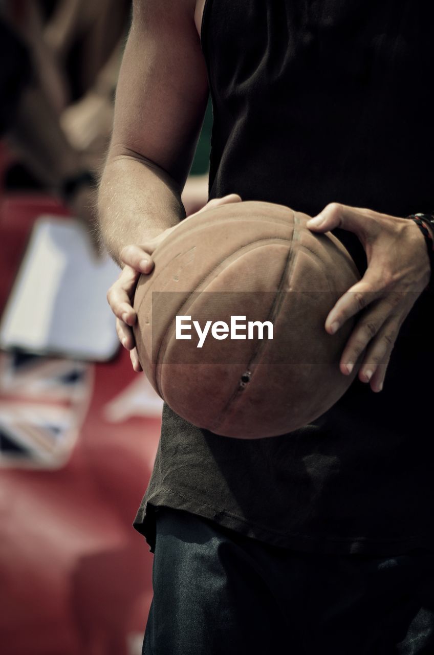 Midsection of man holding ball while standing on court