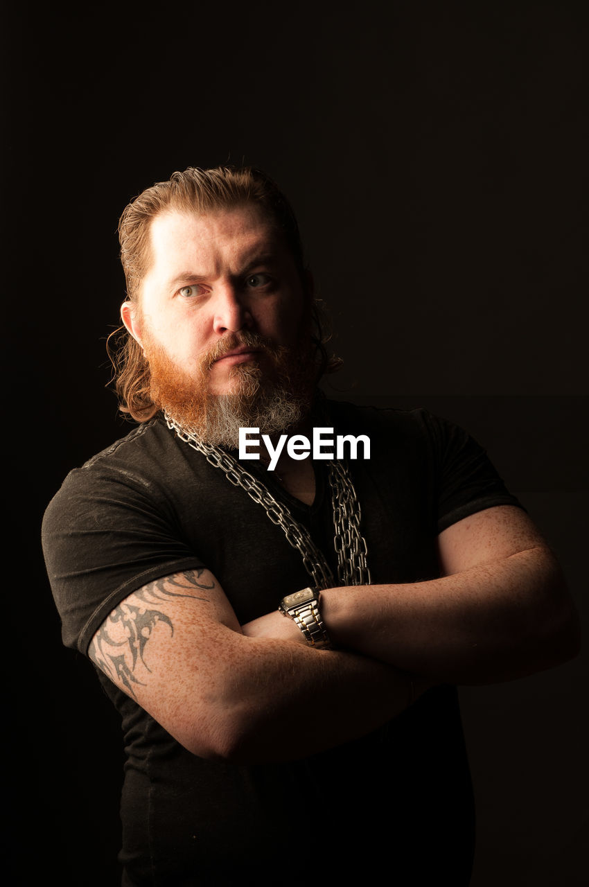 Thoughtful mid adult man with beard standing against black background