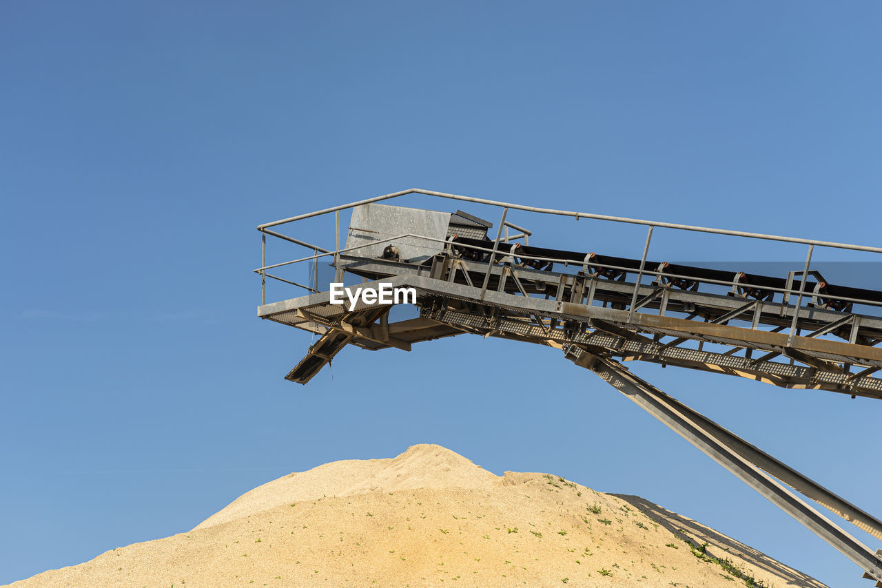 Conveyor belt over heaps of gravel against the blue sky at an industrial cement plant.