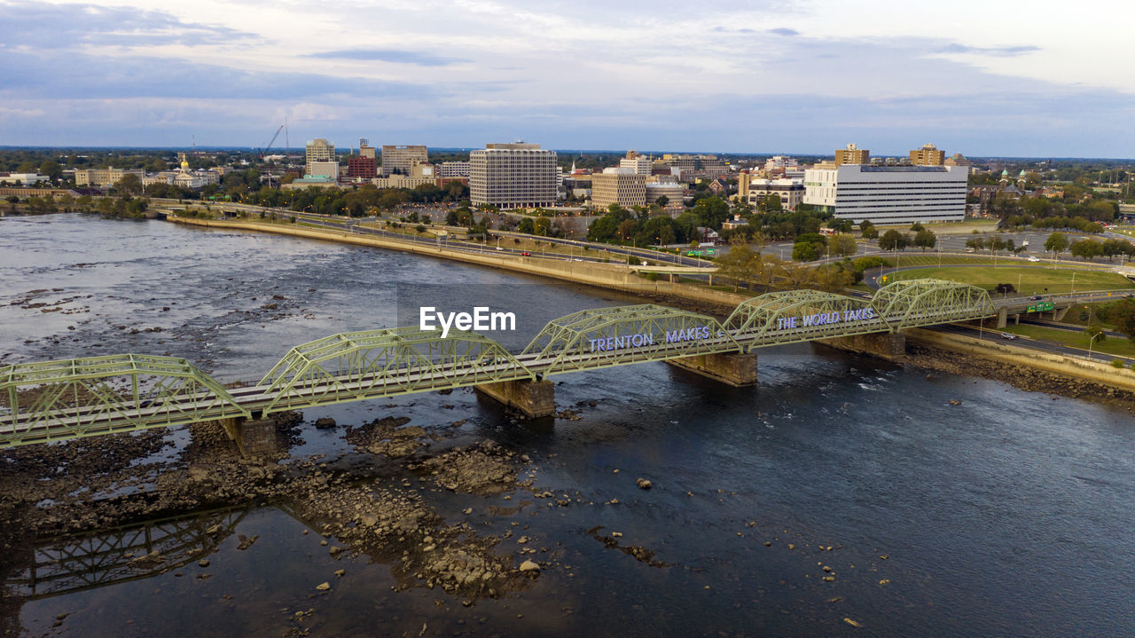 Bridge over river by buildings in city against sky