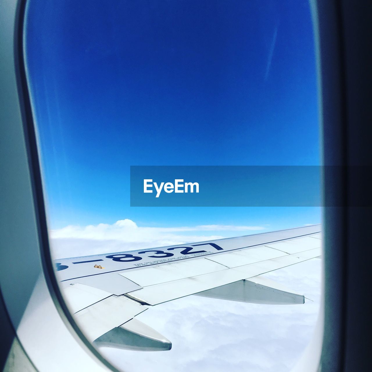 CLOSE-UP OF AIRPLANE WING AGAINST BLUE SKY SEEN FROM WINDOW