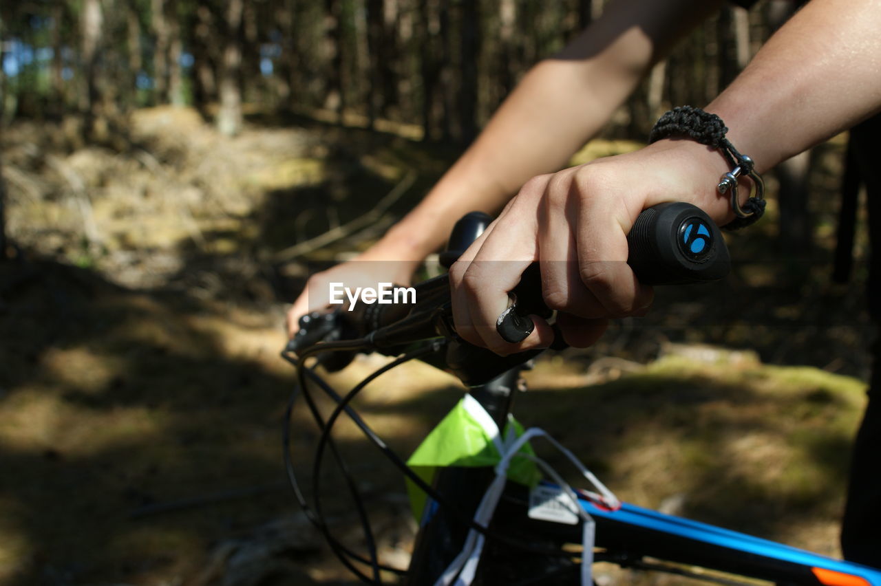 Cropped hands of person holding bicycle handlebar in forest