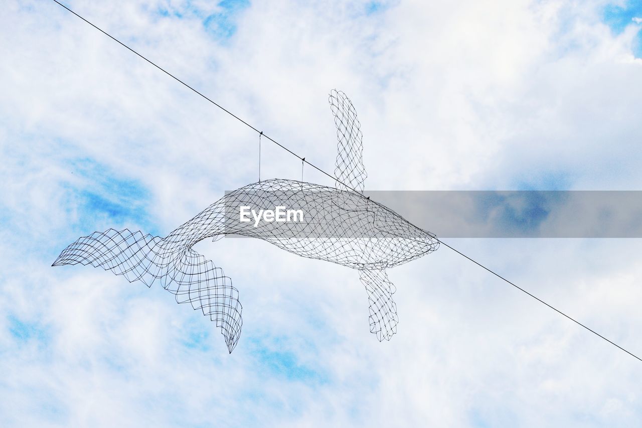 Low angle view of metallic fish decor hanging from cable against sky
