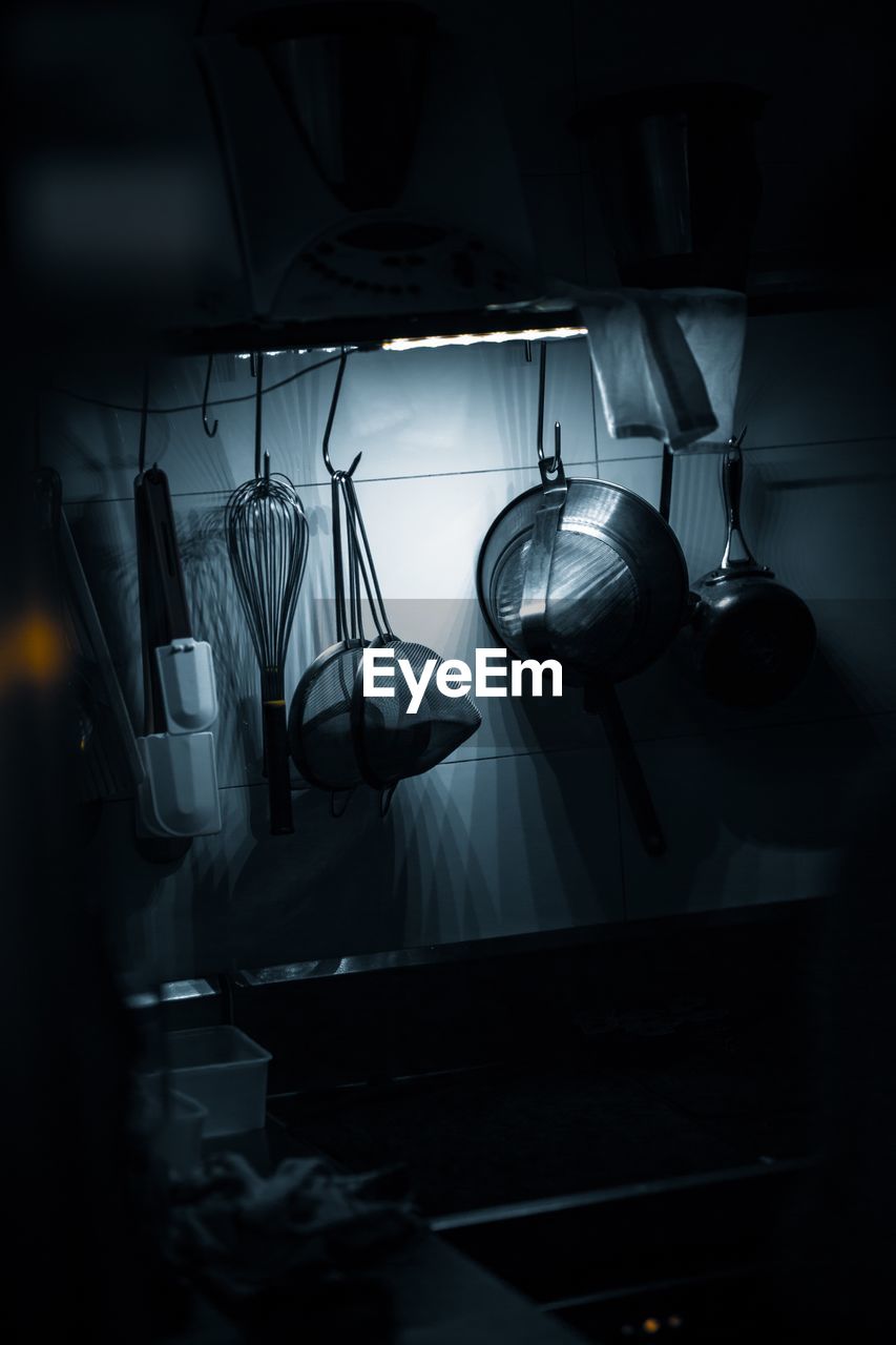 Close-up of kitchen utensils hanging at home in darkroom