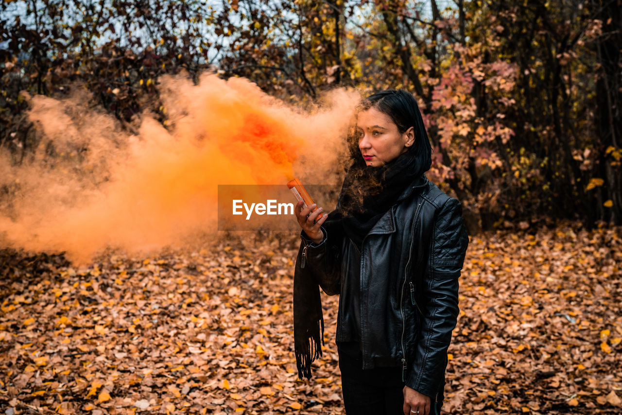 Young woman holding distress flare while standing in forest during autumn