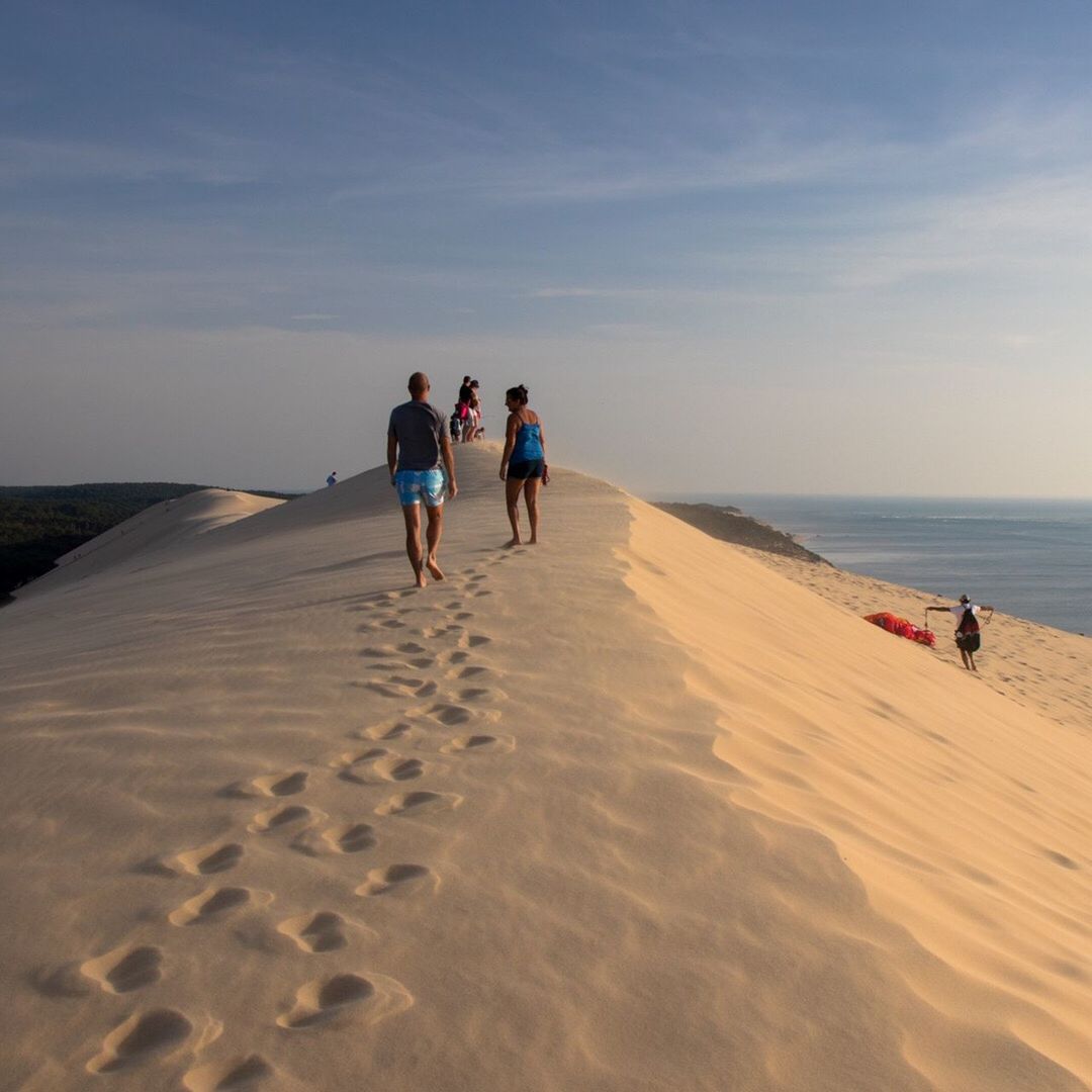 REAR VIEW OF FRIENDS WALKING ON SAND AT BEACH