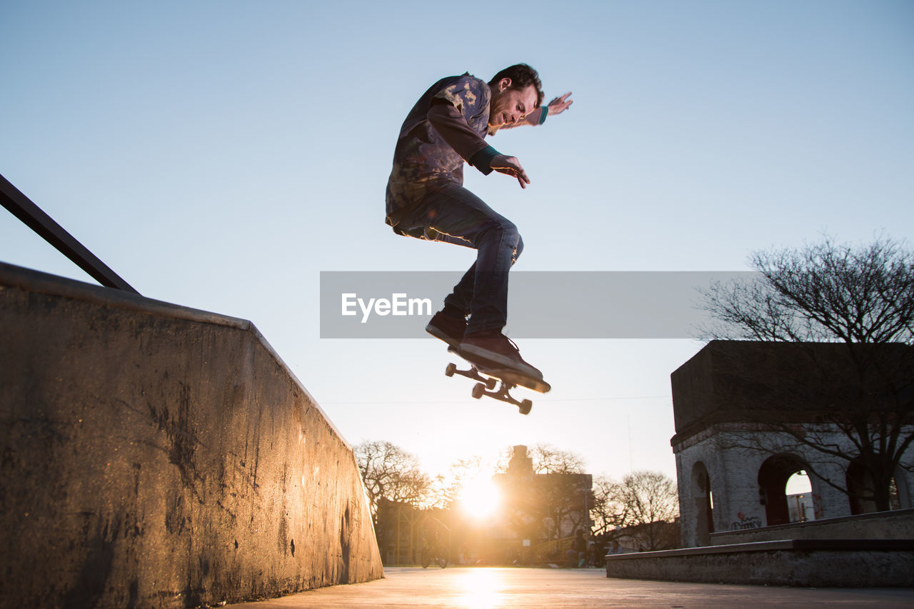 Full length man jumping with skateboard in mid-air against clear sky