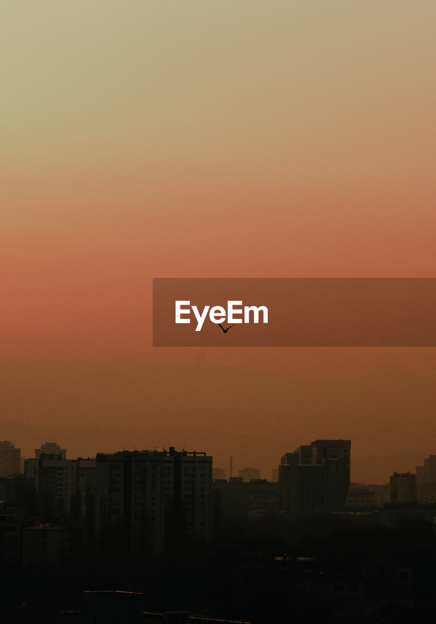 SILHOUETTE OF BUILDINGS AGAINST ORANGE SKY