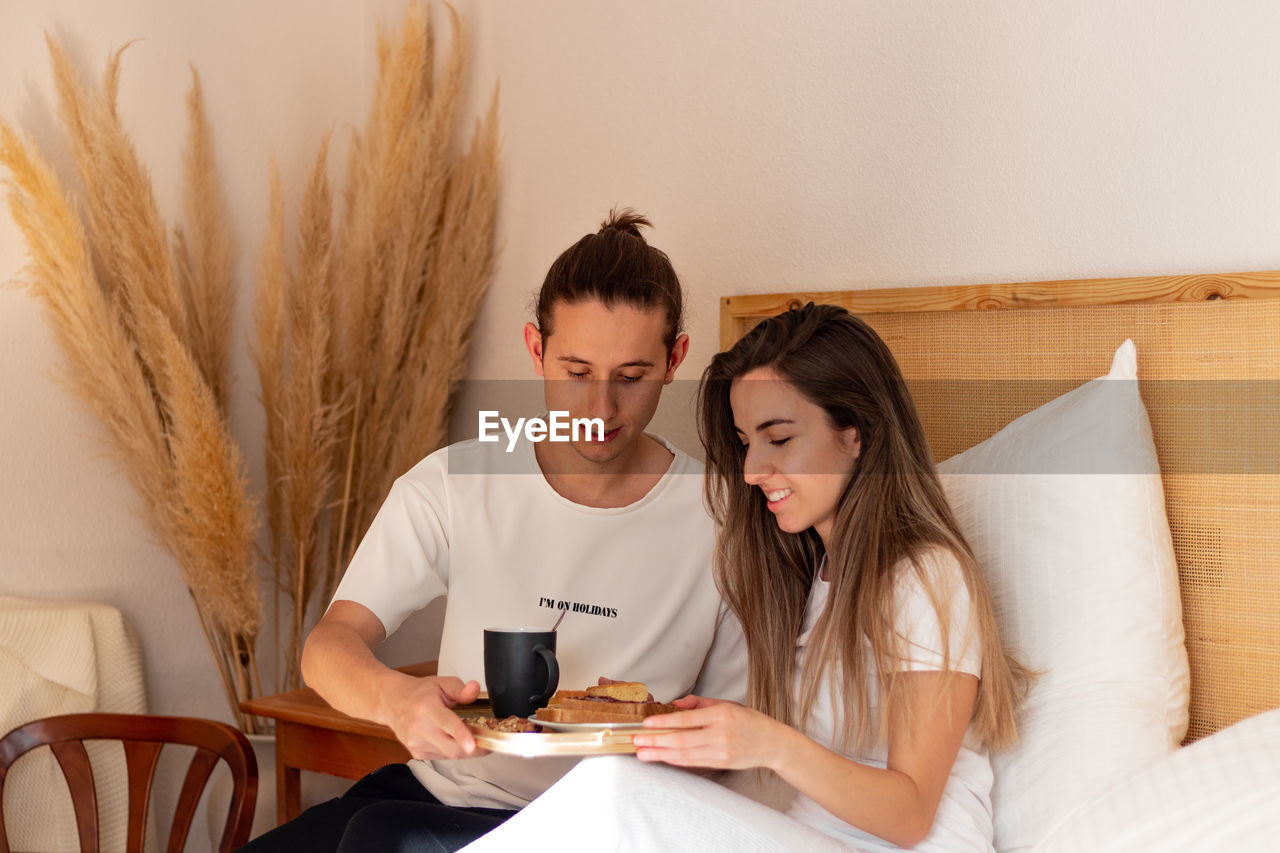 Apreciative young woman beacuse of her boyfriend surprised in bed. happy couple having breakfast