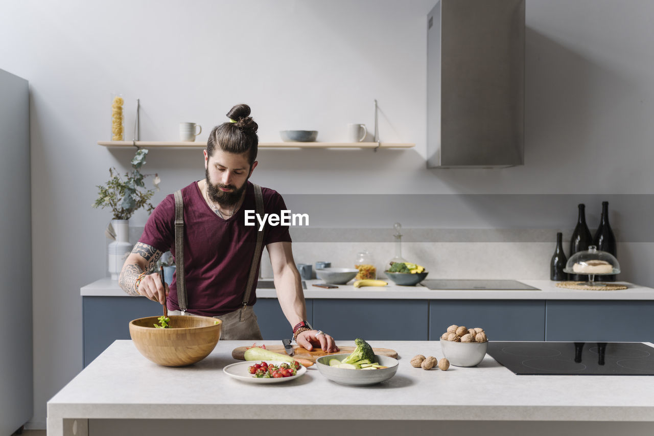 Mid adult man preparing salad while standing by kitchen island