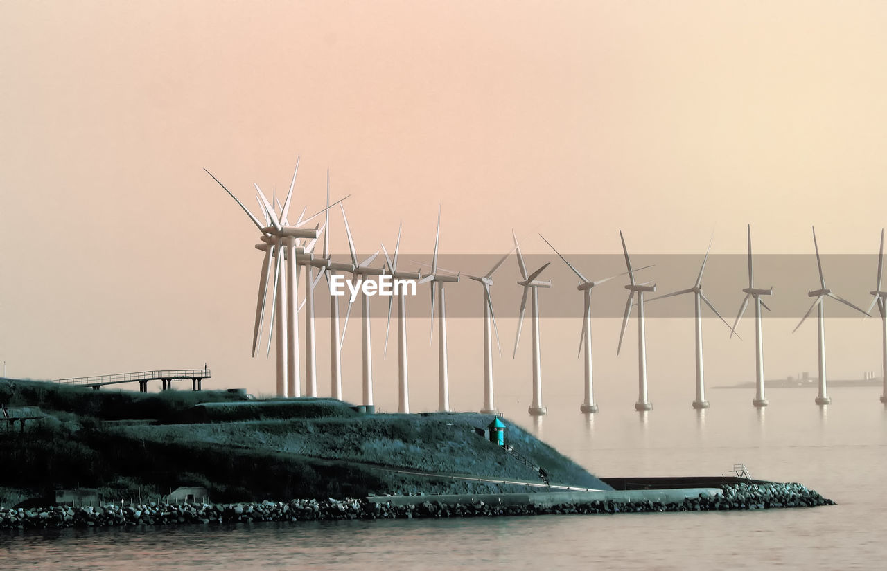 Wind turbines in river against clear sky at sunset