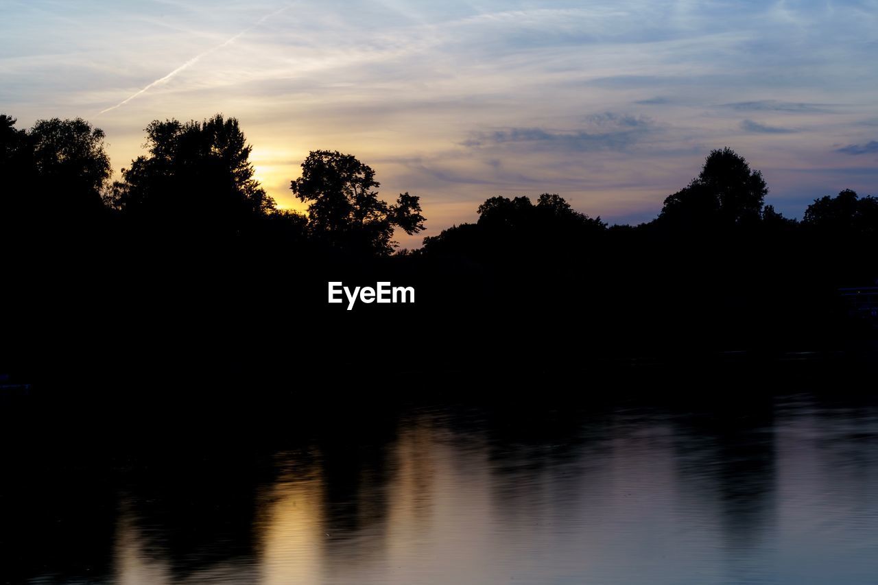 Silhouette trees by lake against sky during sunset