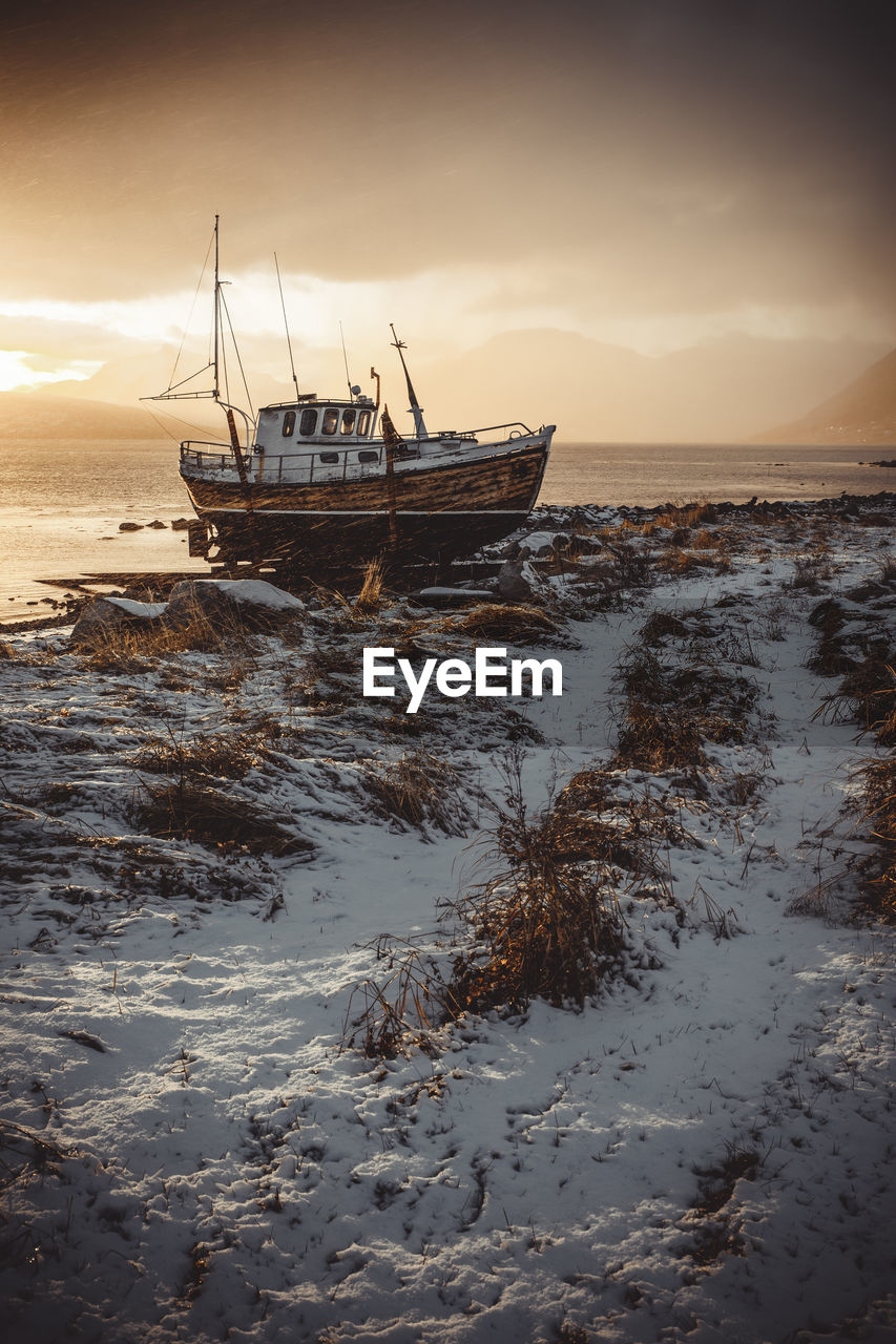 Norwegian wooden boat beached at sunset with snow