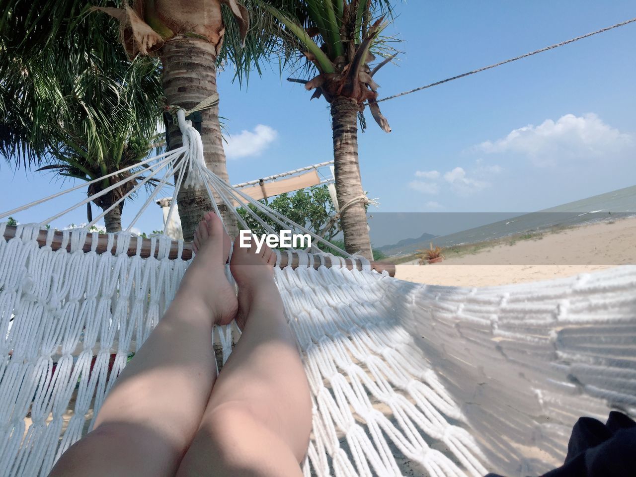 Low section of woman relaxing on hammock at beach against sky