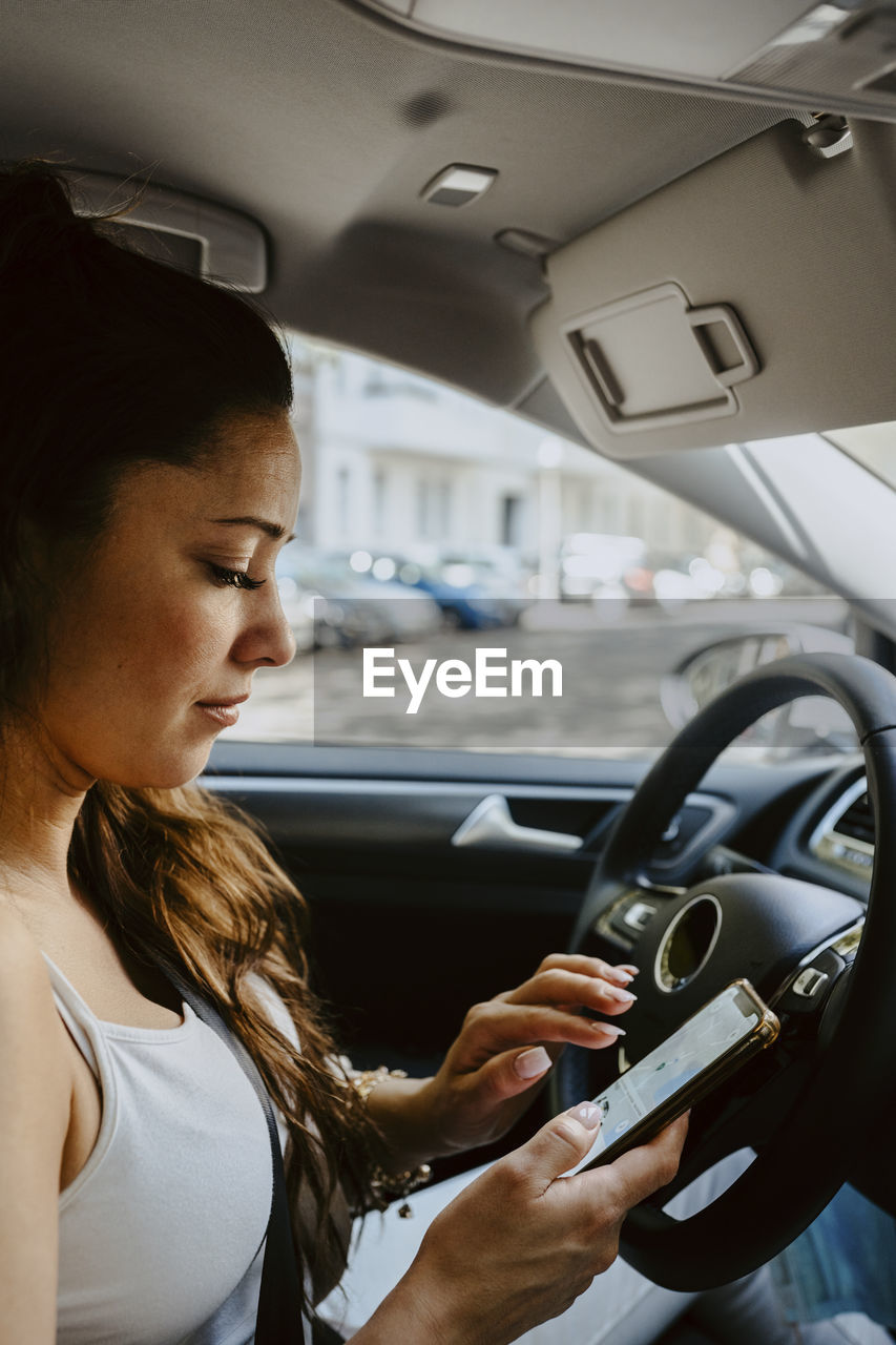 Mid adult woman using map on mobile phone while sitting in electric car