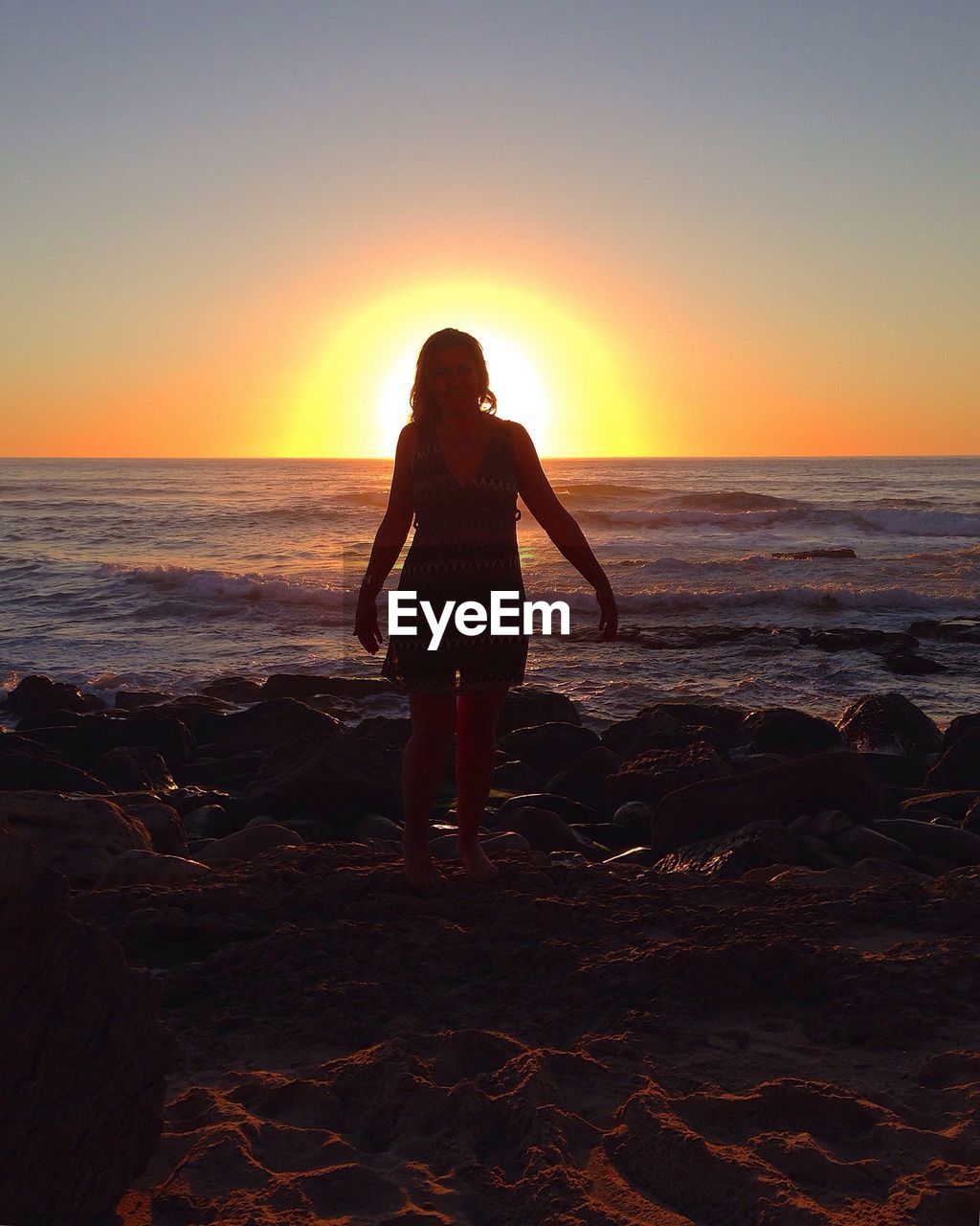 SILHOUETTE OF WOMAN STANDING ON BEACH DURING SUNSET