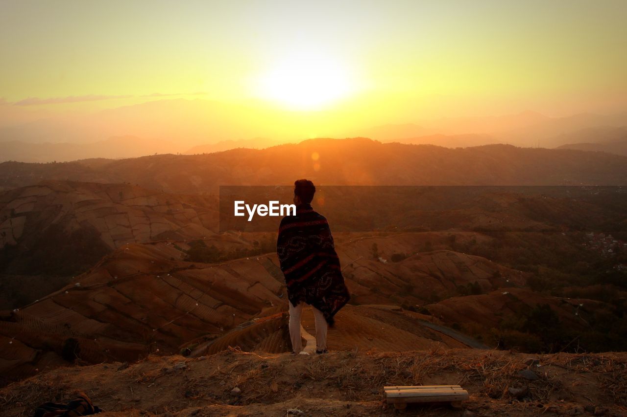 Rear view of man standing on mountain during sunset