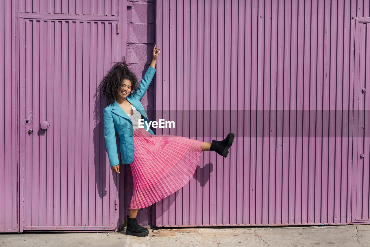 Smiling young woman while dancing by metallic purple wall